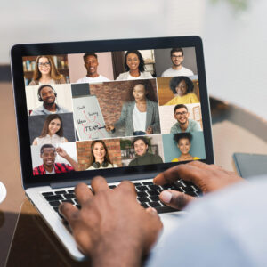 Black Man Web Chatting With Colleagues While Sitting With Laptop In Cafe
